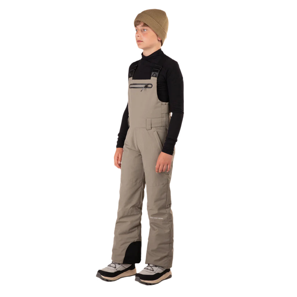 CooperBib-Person wearing beige bib overalls and a black long-sleeve shirt on a white background