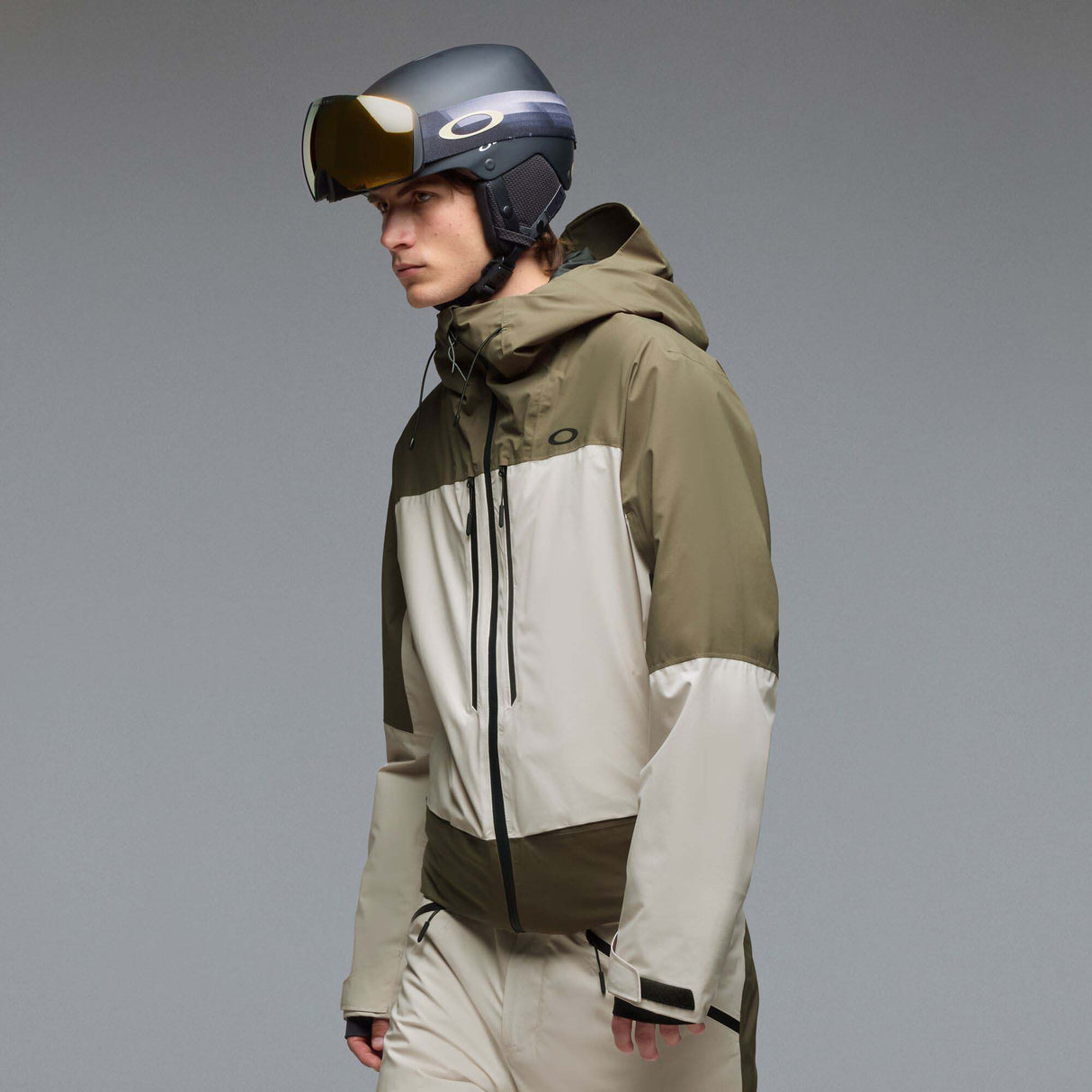 MCanopyProInsulatedJacket-A color-blocked hooded jacket with an olive green upper section, hood, and lower front panel, paired with off-white color-blocked sleeves and a lower front panel. It features a black front zipper, black drawstrings, and a small Oakley logo on the chest.