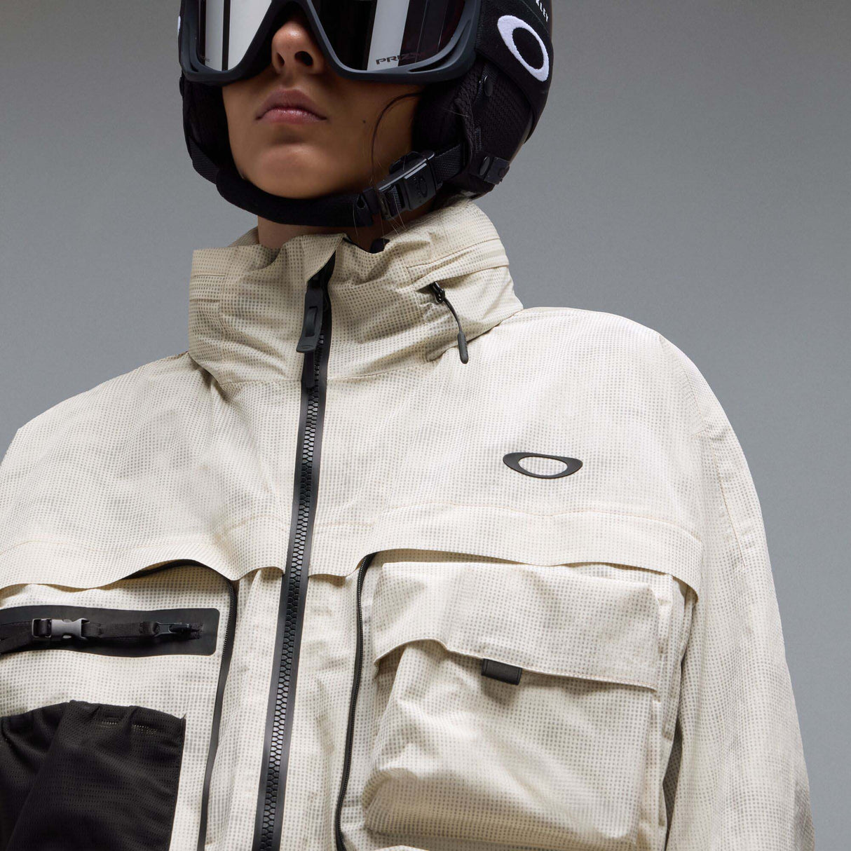 MMthodGlowShellJacket-A light beige technical jacket with black zippers, black piping details, and an Oakley logo on the left chest, displayed against a neutral gray background.