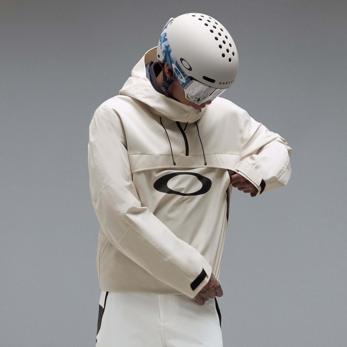 MTimberlineShellAnorak-An off-white hooded anorak jacket with a large black Oakley logo on the chest, displayed against a neutral gray gradient background.