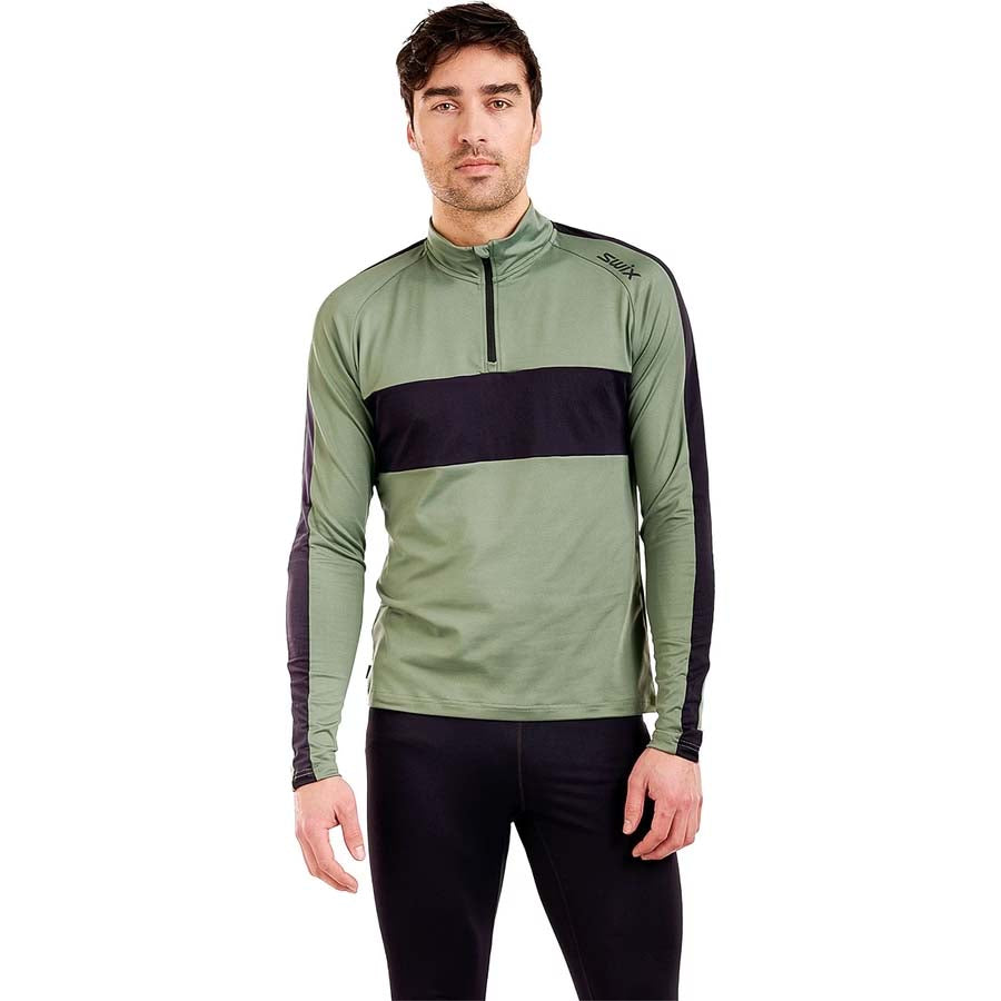 MTista1_2ZipMidlayer- A man wearing a sage green and black long-sleeve quarter-zip athletic pullover, paired with black pants, against a plain white background.