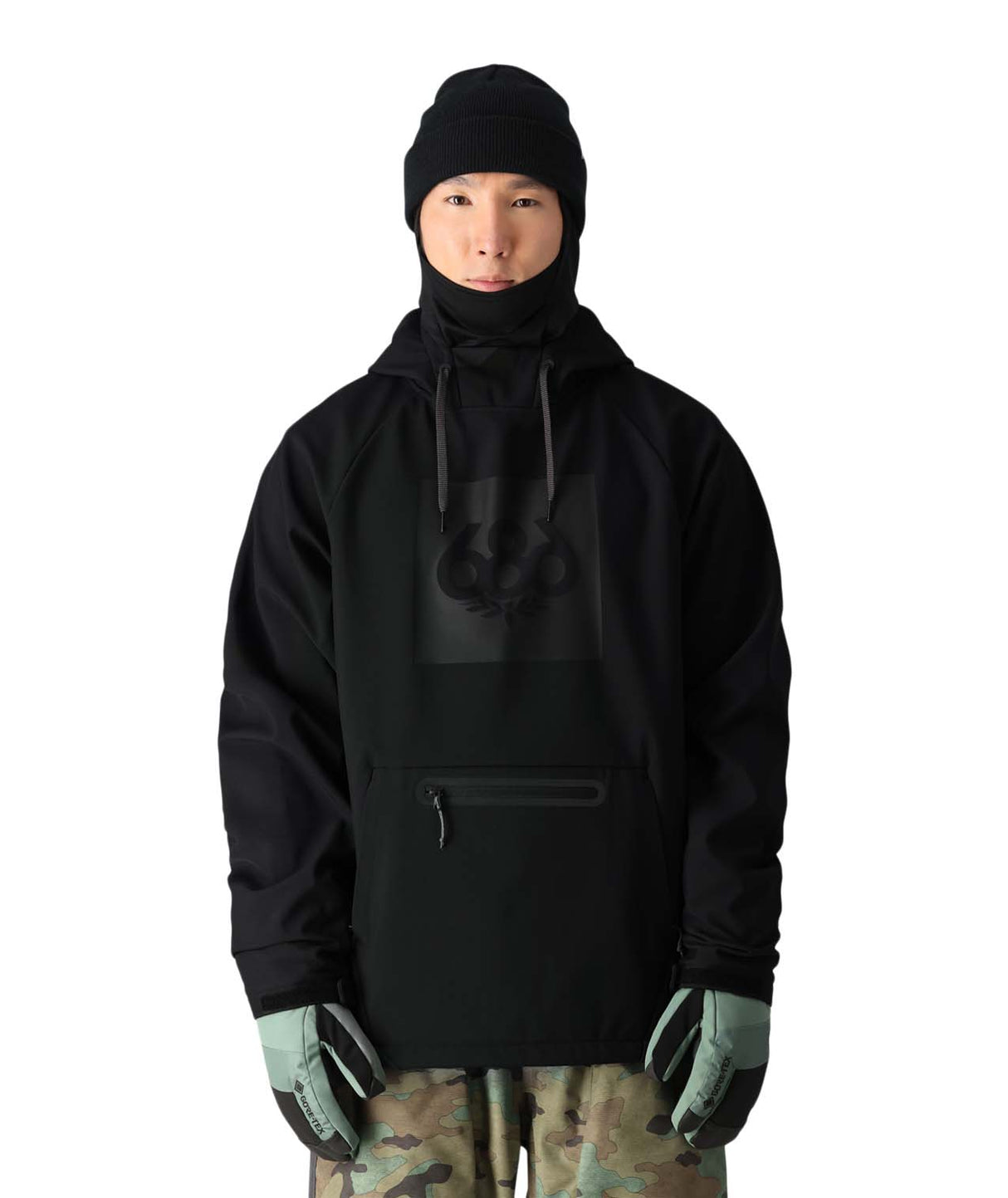 MWaterproofHoody-A model wearing a black hooded jacket with a high neck, black beanie, black gloves, and camouflage pants, shown against a plain white background.