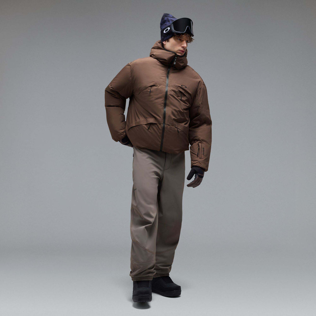 MWintertideSoftshellPant-A pair of gray snow pants with a black belt and a small black Oakley logo on the left thigh, displayed against a neutral gray gradient background.