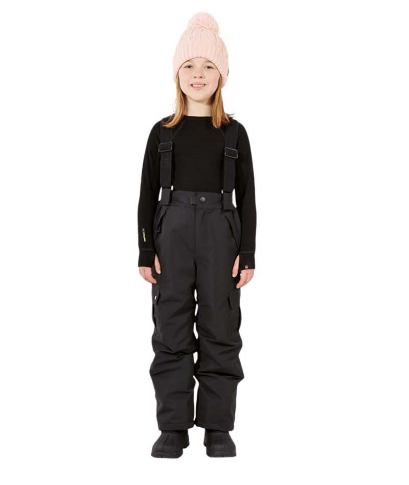 PlutoIIKidsPant-A child model wearing black snow bib overalls with suspenders, a black long-sleeve top, and a light pink knit beanie, standing against a solid white background.
