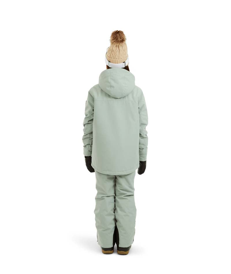 RumbleJacket- A smiling girl wearing a light sage green snowboard jacket, matching snow pants, black gloves, and a knit beanie with ski goggles, standing against a plain white background.