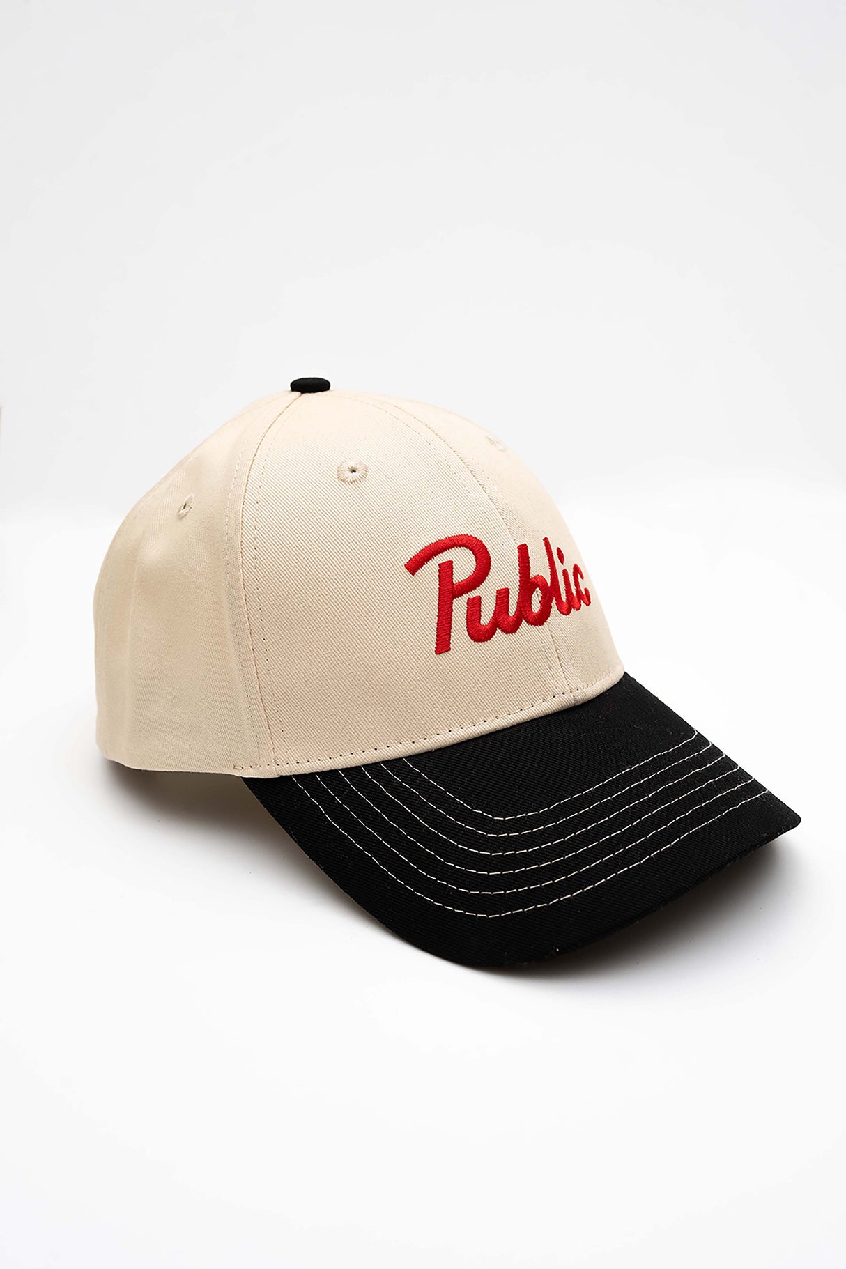 ScriptCap-A baseball cap with a cream-colored crown and a black curved brim, featuring the word 'Public' embroidered in red script on the front. The cap is photographed on a seamless white background.
