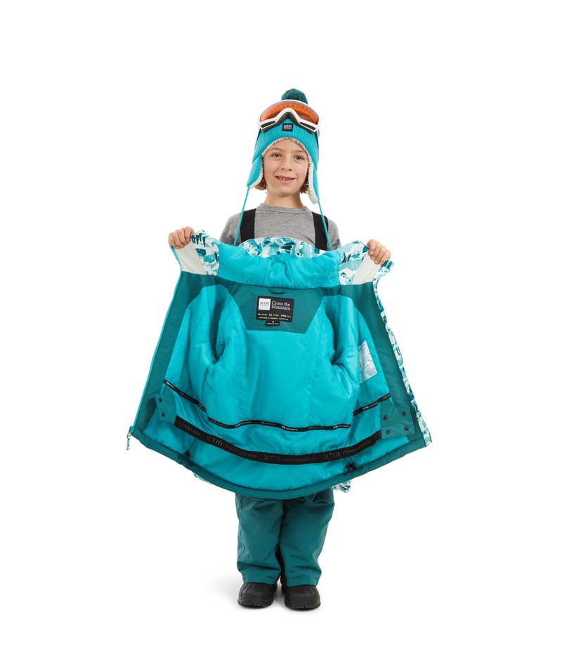 SnowballJacket-A child wearing a winter ski outfit consisting of a light blue and white camouflage-patterned jacket, teal snow pants, a matching teal beanie with orange goggles, and blue gloves, standing against a plain white background.