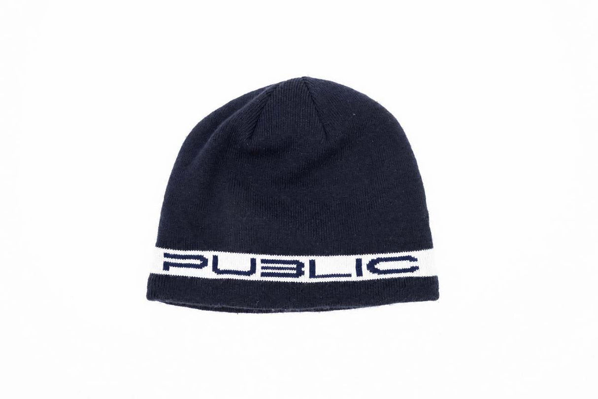 StretchLogoSkully- A dark navy blue knit beanie hat featuring a white horizontal band around the lower half with the word 'PUBLIC' in navy lettering, shown against a plain white background.