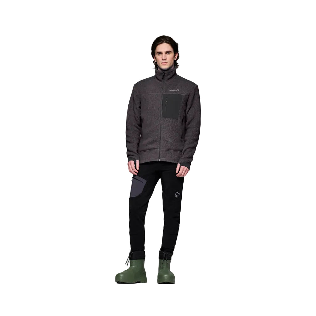 TrollveggenWarm3Jkt_-Person wearing a dark gray jacket, black pants, and green boots on a white background