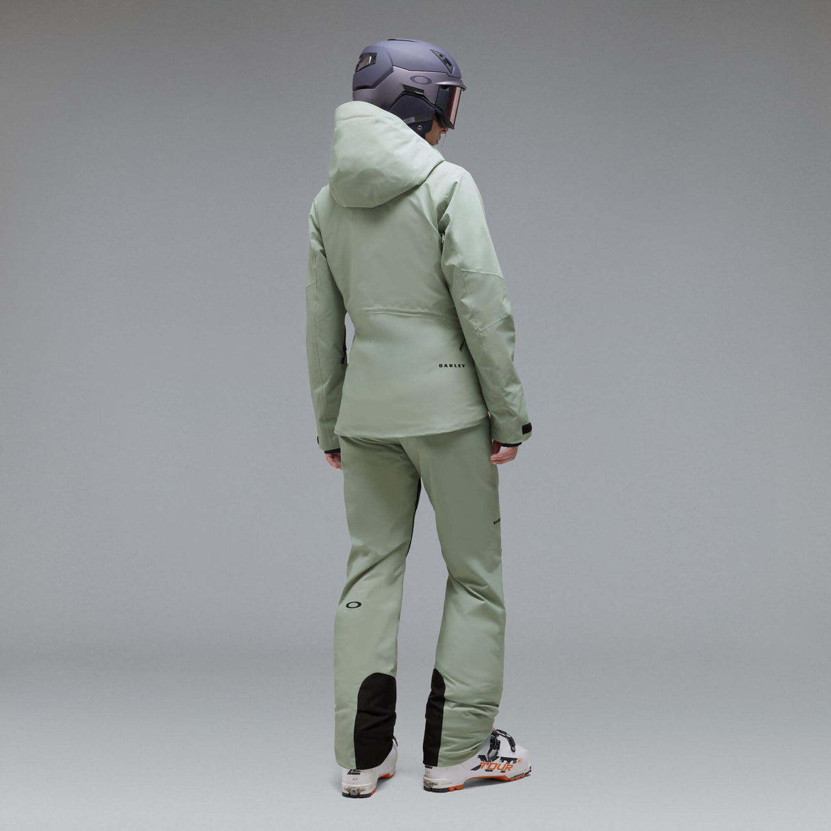 WCanopyInsulatedJacket-A light sage green hooded jacket with black zipper and drawstring details, displayed on a neutral gray background. The Oakley logo is visible on the left chest.