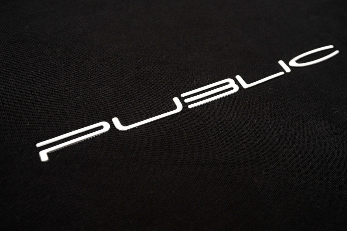 WarpCrewneck-A close-up of a black textured surface featuring the word 'PUBLIC' in a stylized white sans-serif font.