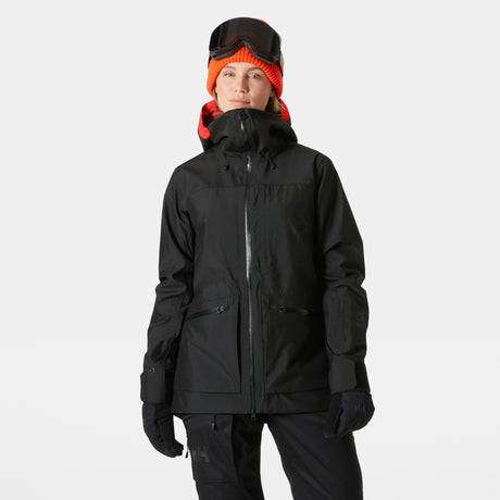 Powderqueen 3.0 Jacket-A woman wearing a black Helly Hansen Powderqueen 3.0 ski and snowboard jacket with a hood, along with black pants, gloves, and a red beanie.