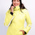 AthenaWomensInsulatedJacket-A woman wearing a bright yellow ski jacket with white side stripes, white ski pants, a black beanie, and blue ski goggles, posing against a light gray studio background.