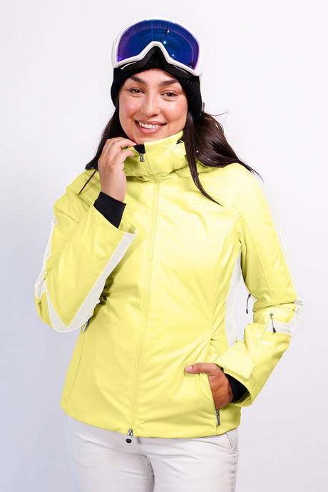 AthenaWomensInsulatedJacket-A woman wearing a bright yellow ski jacket with white side stripes, white ski pants, a black beanie, and blue ski goggles, posing against a light gray studio background.