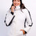 AthenaWomensInsulatedJacket-A woman wearing a white ski jacket with black sleeve stripes, white ski pants, a black beanie, and blue ski goggles, posing against a light gray studio background.
