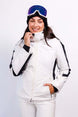 AthenaWomensInsulatedJacket-A woman wearing a white ski jacket with black sleeve stripes, white ski pants, a black beanie, and blue ski goggles, posing against a light gray studio background.