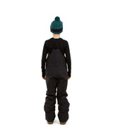 BaileyPant-A child model wearing black snow bib overalls, a black long-sleeve shirt, a dark green beanie with ski goggles, and black snow boots, standing against a solid white background.