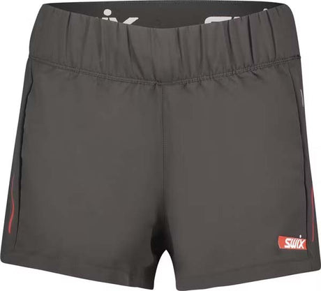 CarbonWomensShorts- Dark gray athletic shorts with an elastic waistband, featuring a white Swix logo on the lower left hem and red side piping details.