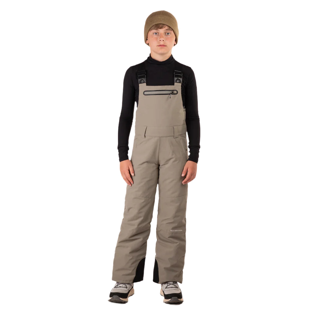CooperBib-Person wearing beige bib overalls and a black long-sleeve shirt on a white background