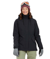 EmeryJacket-A woman wearing a black hooded snowboard jacket, gray gloves, olive green pants, and a maroon knit beanie with ski goggles, standing against a plain white background.