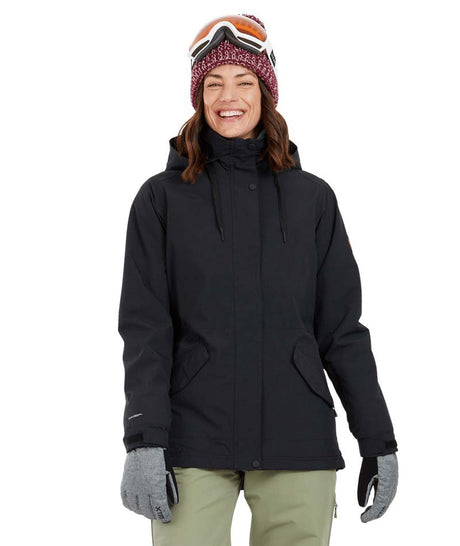 EmeryJacket-A woman wearing a black hooded snowboard jacket, gray gloves, olive green pants, and a maroon knit beanie with ski goggles, standing against a plain white background.