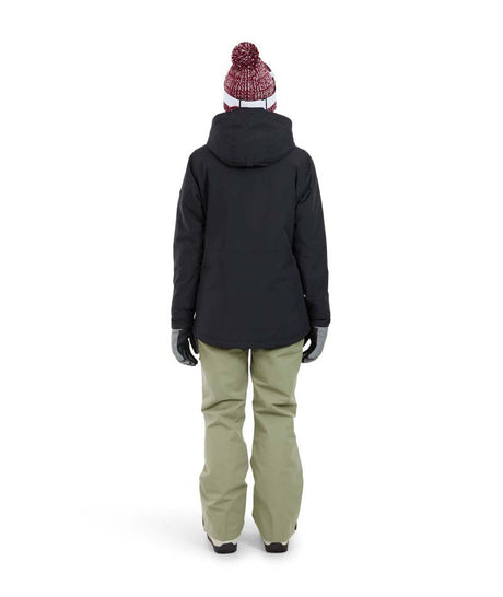 EmeryJacket-A woman wearing a black hooded snowboard jacket, gray gloves, olive green pants, and a maroon knit beanie with ski goggles, standing against a plain white background.