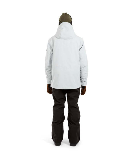 ExposureJacket-A man wearing a light gray ski jacket with black zippers, a dark beanie with goggles, and brown gloves, standing against a plain white background.