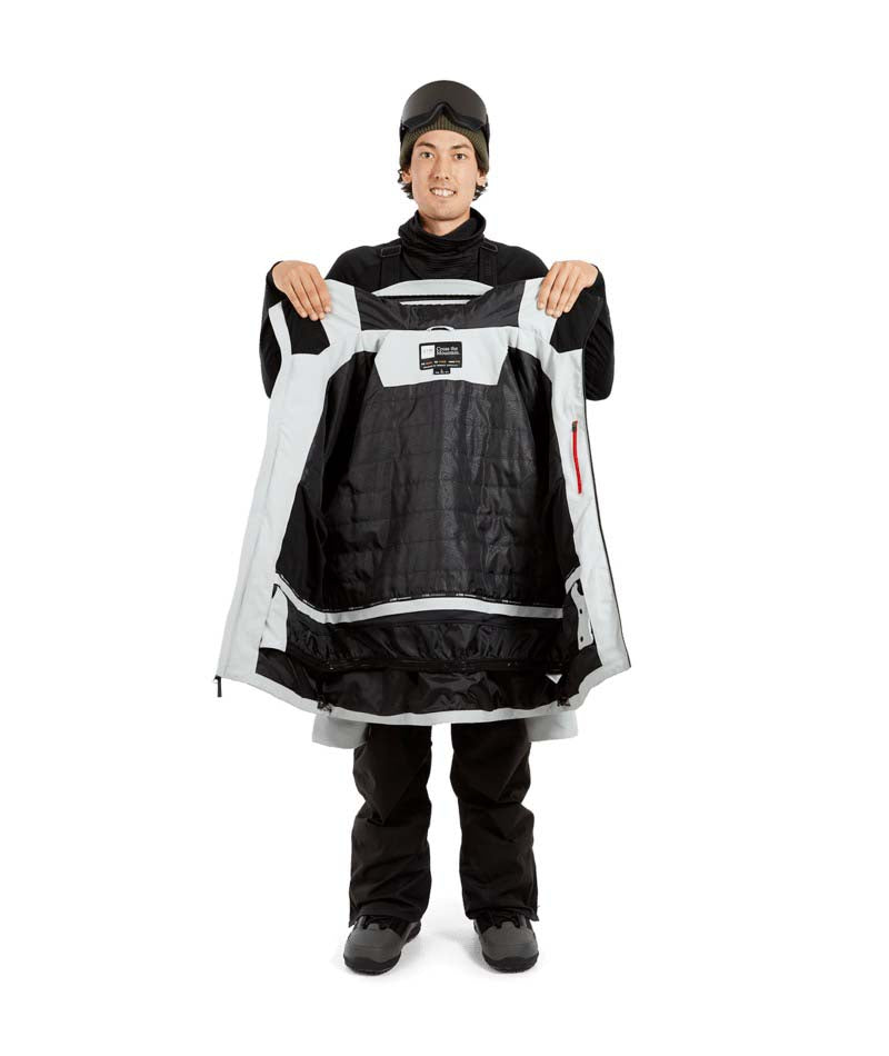 ExposureJacket-A man wearing a light gray ski jacket with black zippers, a dark beanie with goggles, and brown gloves, standing against a plain white background.