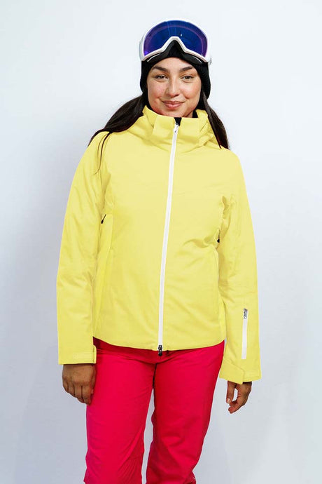 GaiaWomensInsulatedJacket-A woman modeling a bright yellow ski jacket with a white zipper, paired with red ski pants, blue goggles, and a black beanie against a light gray studio background.