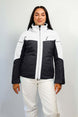 HelenaWomensInsulatedJacket-A woman modeling a colorblock ski jacket in white and black, paired with white ski pants, against a light gray studio background.