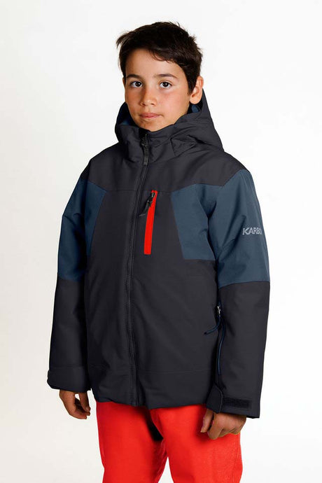 HydraBoysInsulatedJacket-A child wearing a Karbon ski jacket in dark gray and navy blue with a red zipper accent, paired with bright red pants, against a plain white studio background.