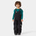 KidsRider2InsulatedBib- A young child wearing black Helly Hansen snow bib overalls over a teal long-sleeve shirt, standing against a light gray studio background.
