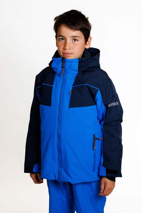 KrakenBoysInsulatedJacket-A young boy wearing a blue and navy Karbon ski jacket and matching blue ski pants, standing against a plain white studio background.