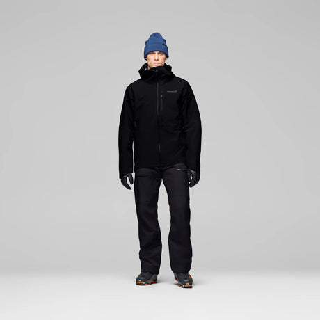 LofotenGore-TexJkt-Person wearing a black jacket, pants, and blue beanie on a gray background
