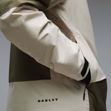 MCanopyProInsulatedJacket-A color-blocked hooded jacket with an olive green upper section, hood, and lower front panel, paired with off-white color-blocked sleeves and a lower front panel. It features a black front zipper, black drawstrings, and a small Oakley logo on the chest.