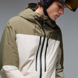 MCanopyProInsulatedJacket-A color-blocked hooded jacket with an olive green upper section, hood, and lower front panel, paired with off-white color-blocked sleeves and a lower front panel. It features a black front zipper, black drawstrings, and a small Oakley logo on the chest.