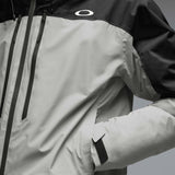 MCanopyProInsulatedJacket-A colorblock hooded jacket with a black upper section and sleeves, a light gray midsection, and a black lower section, featuring a full-zip front and a small white Oakley logo on the chest.