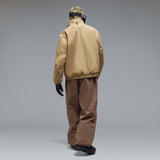 MChannelJacket-A beige lightweight zip-up jacket with a black front zipper, black side zip pockets, and a small black Oakley logo on the left chest, displayed against a neutral gray gradient background.
