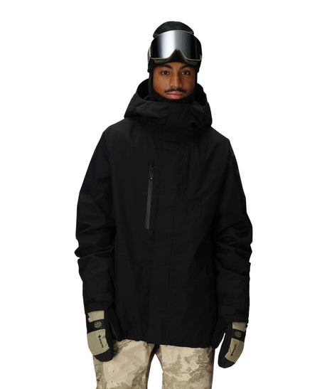 MGore-texCoreShellJacket-Person wearing a black snow jacket, goggles, and camouflage pants on a white background