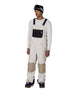 MHotLapInsulatedBib- A man modeling off-white snow bib overalls with beige knee patches, worn over a white long-sleeve shirt and paired with black snow boots and goggles, on a solid white background.