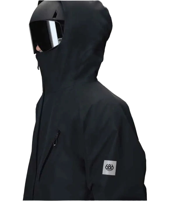MHydraThermagraphJacket-A man wearing a black ski jacket with black zippers, black gloves, a cream neck gaiter, and a black beanie with goggles, photographed against a plain white background.