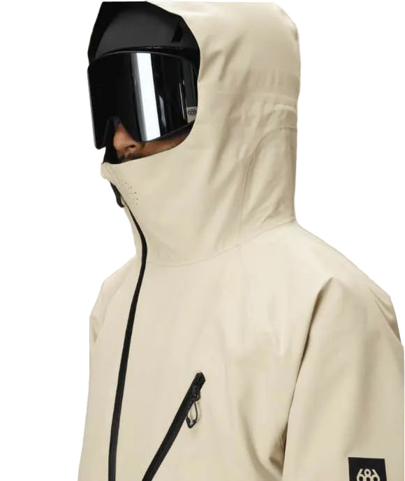 MHydraThermagraphJacket-A man wearing a color-blocked ski jacket in beige and black, along with black snow pants, gloves, and ski goggles, photographed against a solid white background.