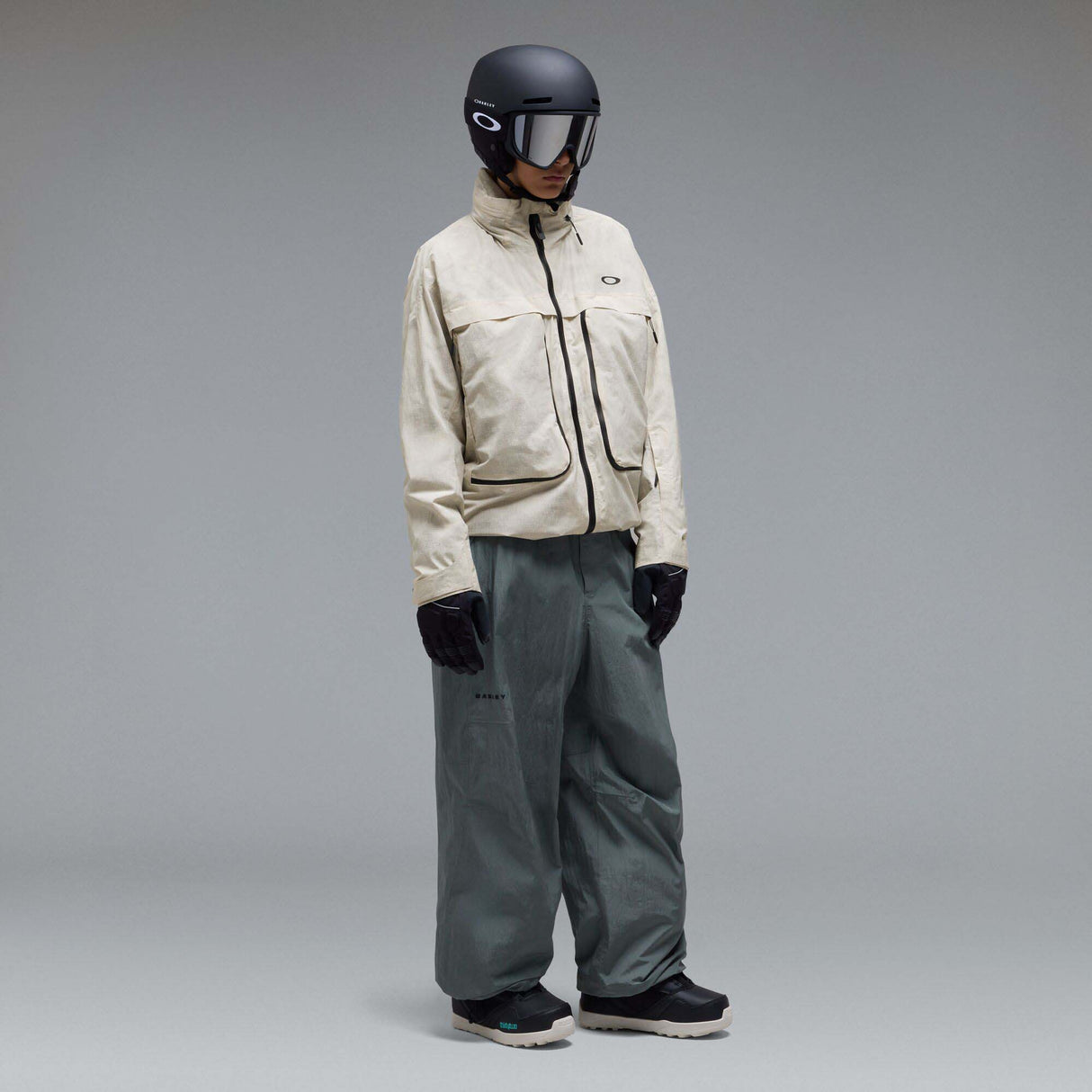 MMthodGlowShellJacket-A light beige technical jacket with black zippers, black piping details, and an Oakley logo on the left chest, displayed against a neutral gray background.