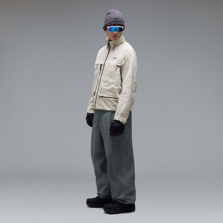 MMthodGlowShellJacket-A light beige technical jacket with black zippers, black piping details, and an Oakley logo on the left chest, displayed against a neutral gray background.