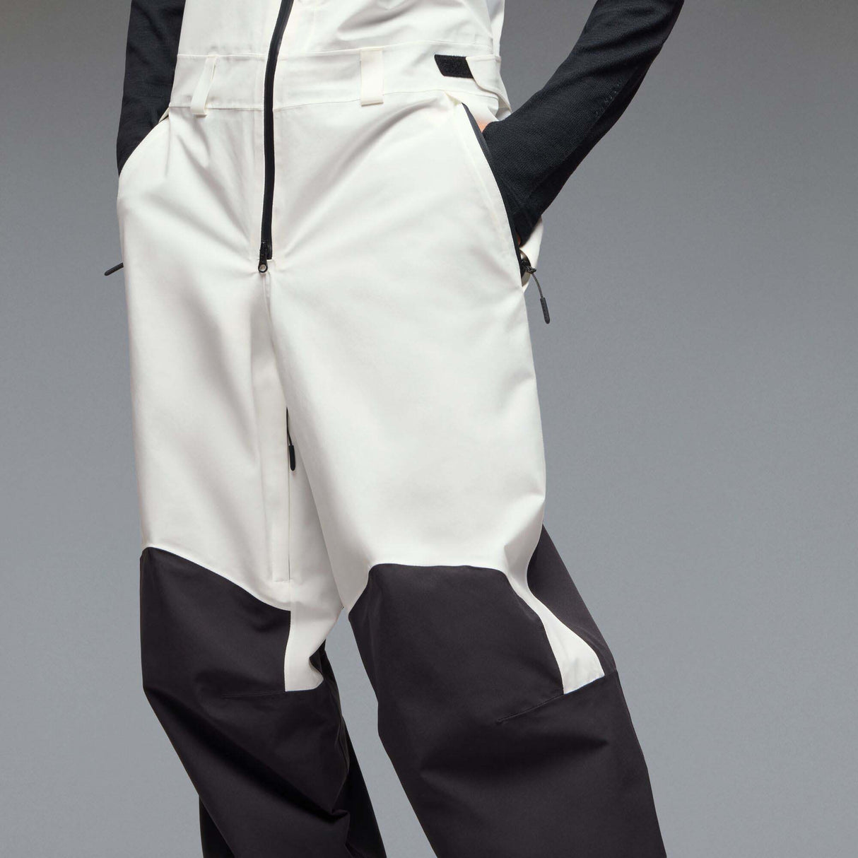 MTimberlineShellBib-A white and black technical snow bib with adjustable shoulder straps, a front zipper, and reinforced lower leg panels, shown against a neutral gray gradient background.