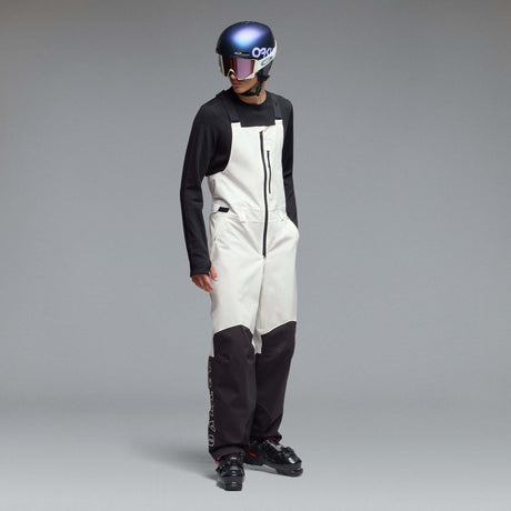 MTimberlineShellBib-A white and black technical snow bib with adjustable shoulder straps, a front zipper, and reinforced lower leg panels, shown against a neutral gray gradient background.