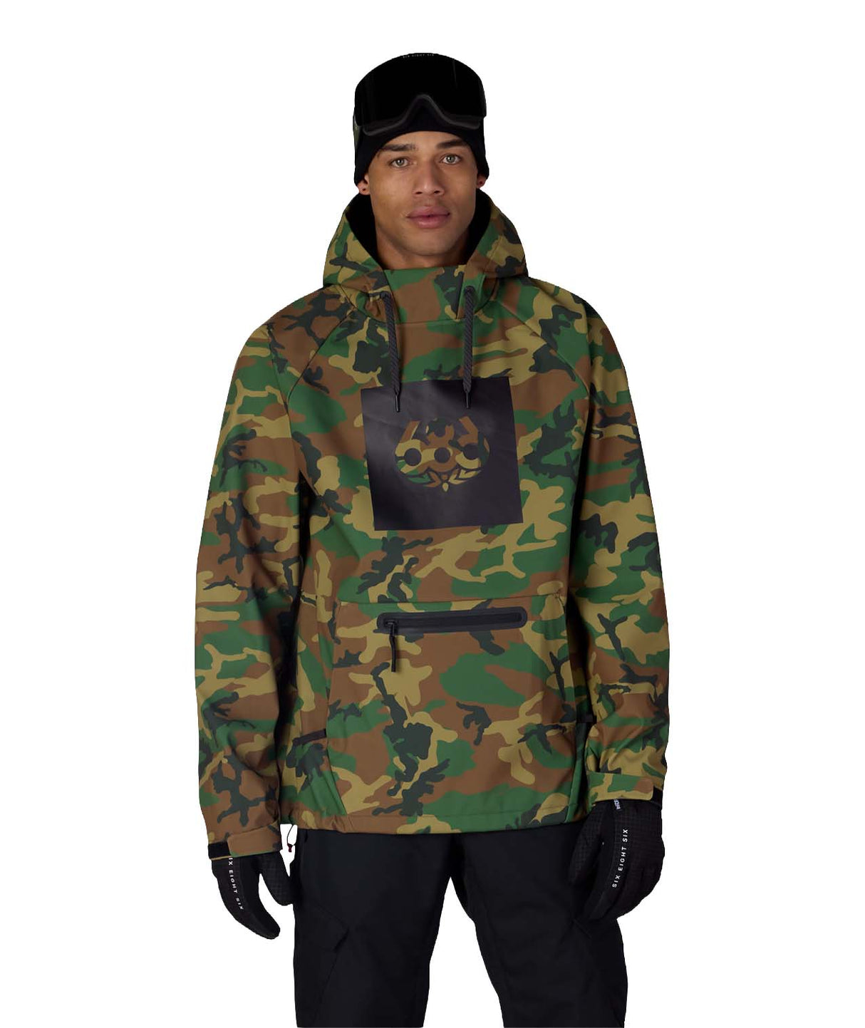 MWaterproofHoody-A man wearing a camouflage hooded jacket with a black chest patch featuring a skull graphic, paired with black pants, gloves, and a black beanie, against a plain white background.