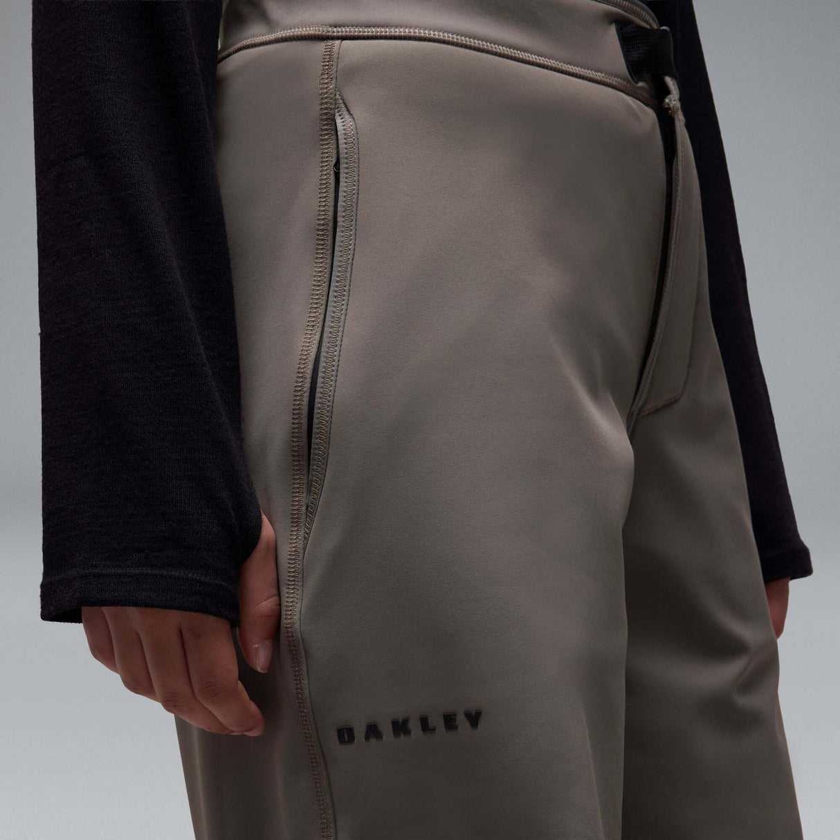 MWintertideSoftshellPant-A pair of gray snow pants with a black belt and a small black Oakley logo on the left thigh, displayed against a neutral gray gradient background.
