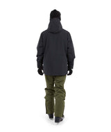 NateJacket-A man wearing a black XTM snowboard jacket, black beanie with green-tinted goggles, black gloves, and olive pants, standing against a solid white background.