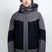 OrionMensInsulatedJacket- A man wearing a Karbon ski jacket in gray and black, a green beanie, and ski goggles, standing against a light gray studio background.